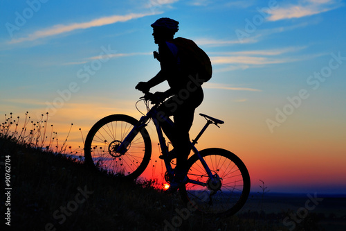 Silhouette of a biker and bicycle on sky background. © Aleksey