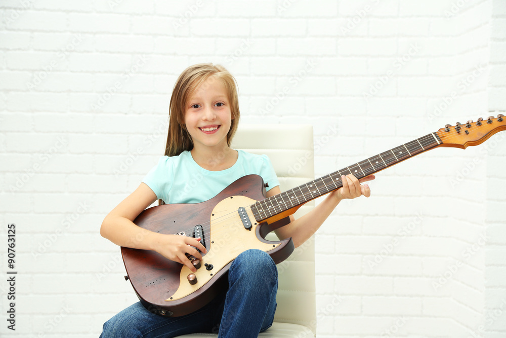 Fototapeta premium Little girl playing guitar on light background