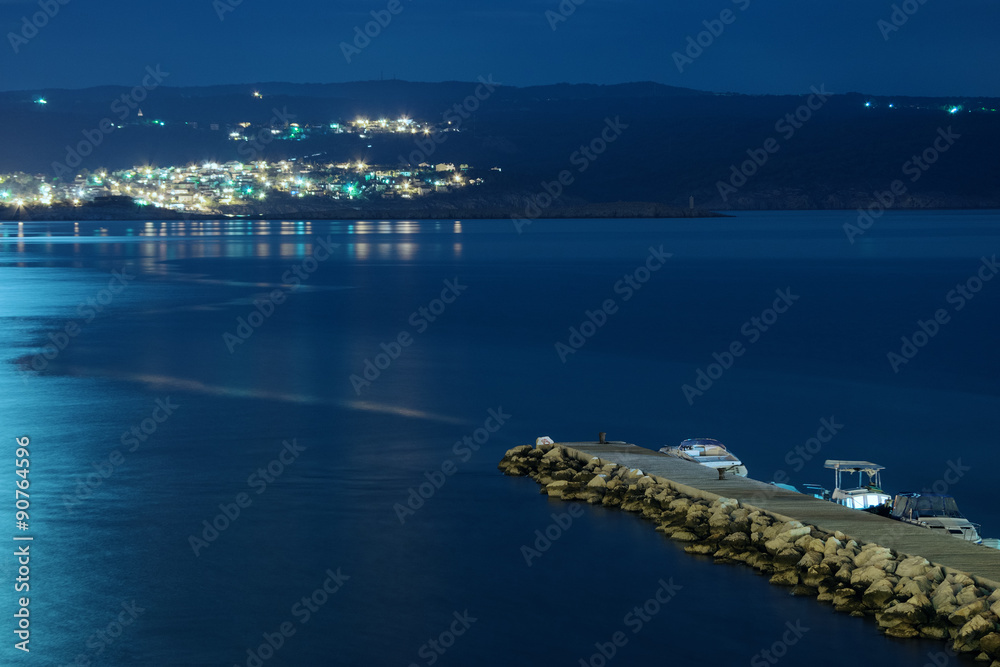 Small dock at night with distant town lights in the background 