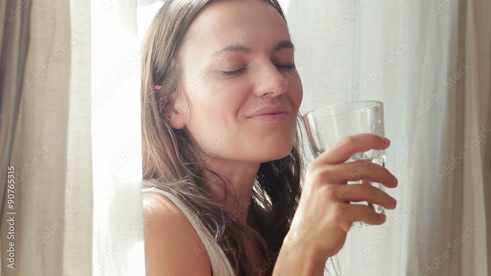 Young beautiful woman drinking water by the window