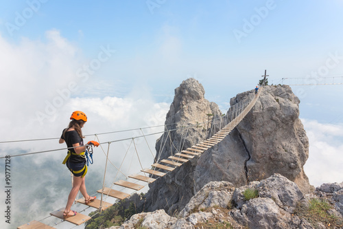 Young woman crossing the chasm on the rope bridge