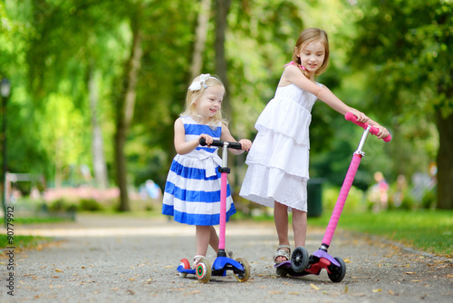 Two little sisters riding their scooters