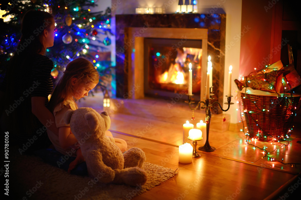 Fototapeta Young mother and daughter sitting by a fireplace on Christmas