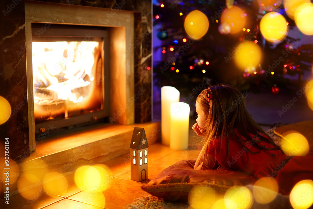 Happy little girl sitting by a fireplace on Christmas eve