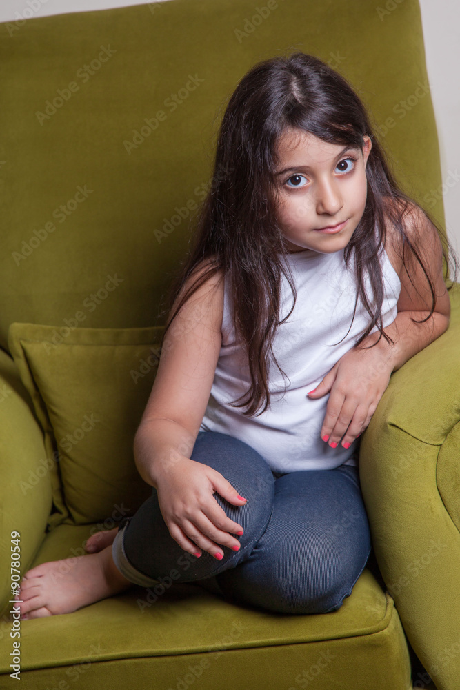 One beautiful happy middle eastern small girl sitting on green chair and smiling