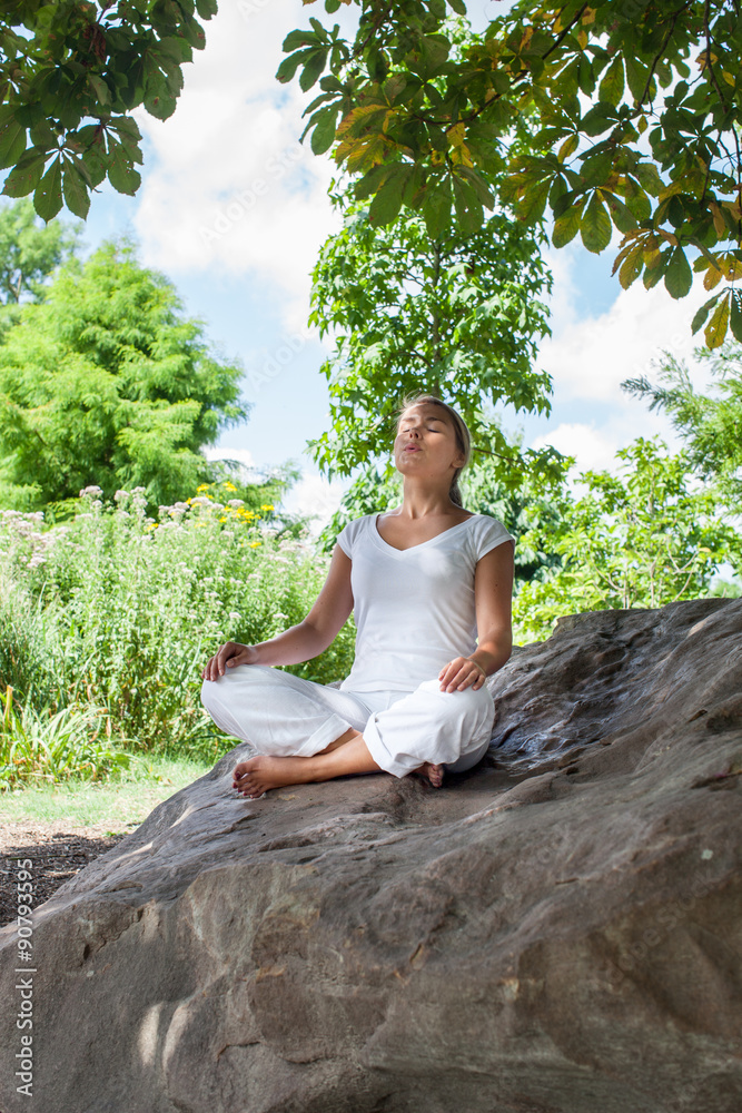outdoors zen exercise - focused young yoga woman escaping in closing eyes,relaxing bare feet on a big stone, summer daylight