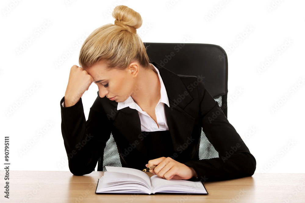 Tired businesswoman writing note by a desk Tired businesswoman writing note by a desk