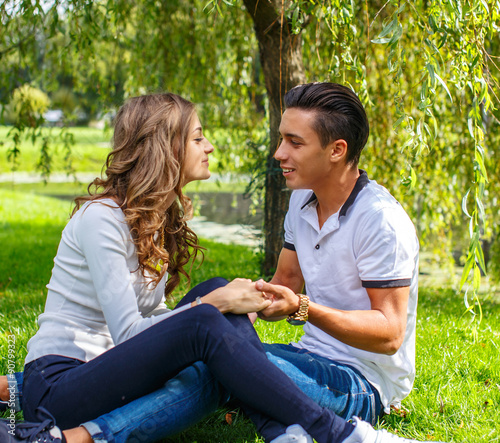 Beautiful young casual couple sitting on grss in a park.