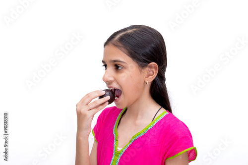 young indian girl eating a gulab jamun {an indian sweet  ) isolated on white with clipping path available photo