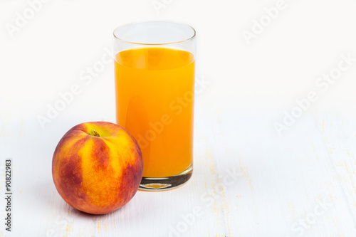 Glass with peach juice and ripe peache on white wooden background