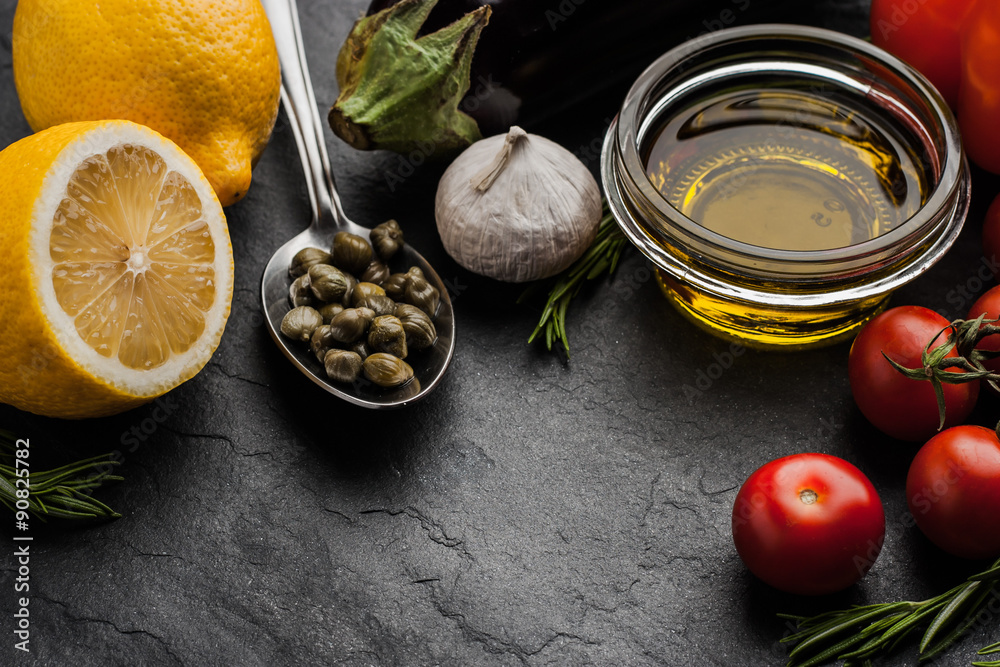 Olive oil with vegetables , lemon and capers on the black stone table Olive oil with vegetables , lemon and capers on the black stone table