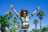 Beautiful funny smiling girl is jumping in palm trees in sunny Barcelona in summer 