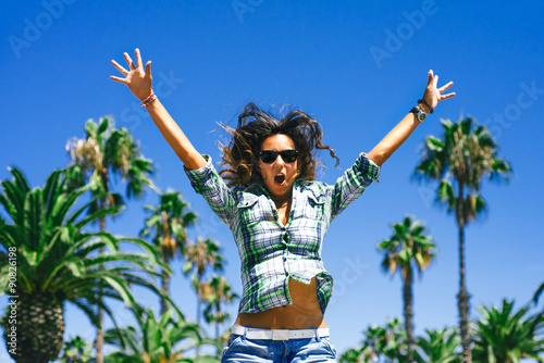 Beautiful funny smiling girl is jumping in palm trees in sunny Barcelona in summer
