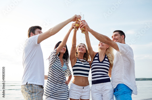 smiling friends clinking bottles on beach