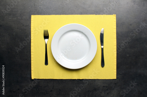 Empty plate, cutlery and yellow placemat on dinning table