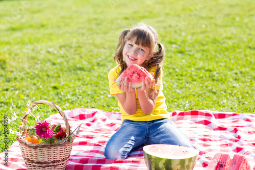 cute little girl eating watermelon on grass in summertime