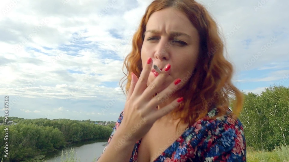 young curly red-haired woman smokes cigarette on the nature young curly red-haired woman smokes cigarette on the nature
