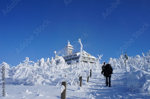Wanderer auf dem Fichtelberg/Das Fichtelberghaus im Winter, traumhafte Kulisse auf dem Fichtelberg im Erzgebirge, dick verschneite Bäume und Büsche und wolkenloser HImmel photo