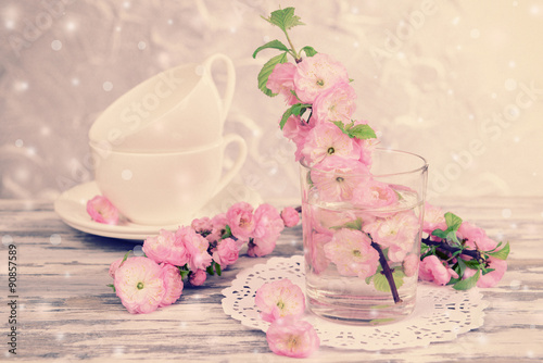 Beautiful fruit blossom in glass and tea cups on table on light background