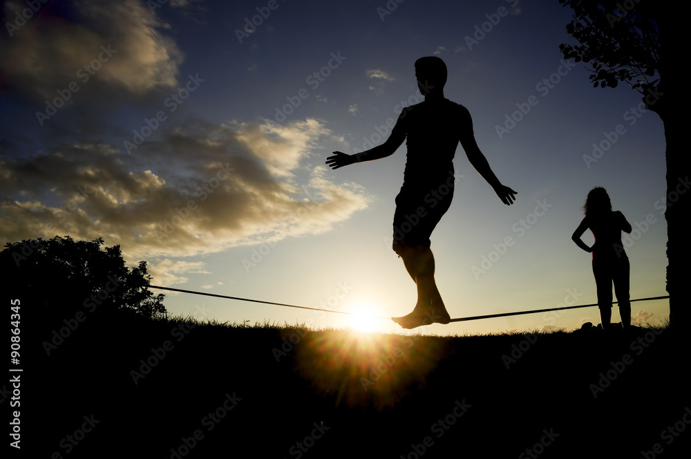 man balancing in slack line , slacklining , and woman looks at him man balancing in slack line , slacklining , and woman looks at him