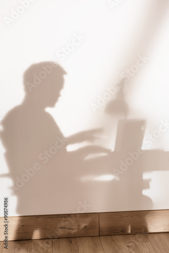 shadow on the wall of a man sitting and working on his laptop