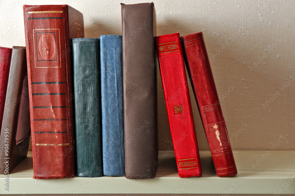 Old books on shelf, close-up, on light wall background Old books on shelf, close-up, on light wall background