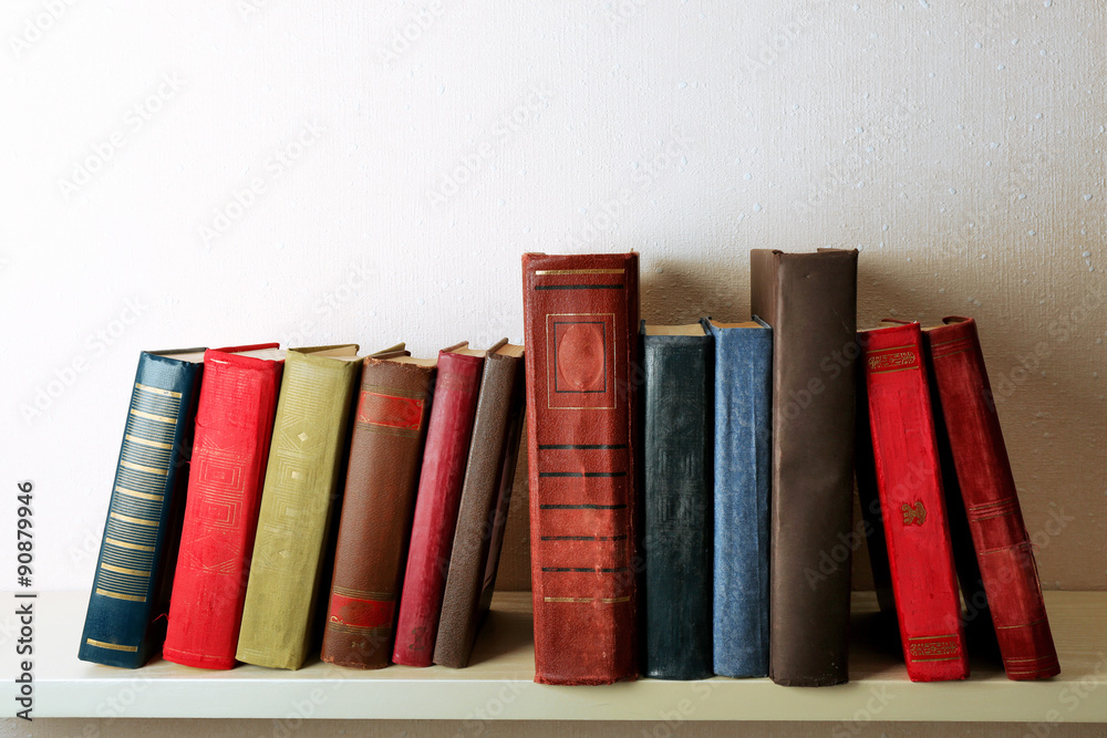Old books on shelf, close-up, on light wall background Old books on shelf, close-up, on light wall background