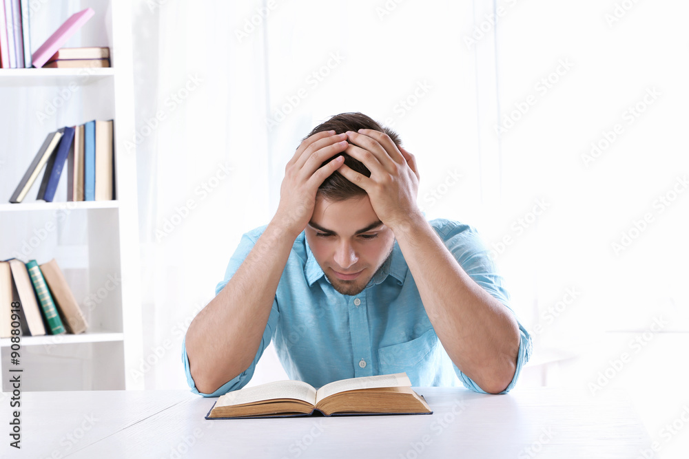 Young man reading book at table in room Young man reading book at table in room