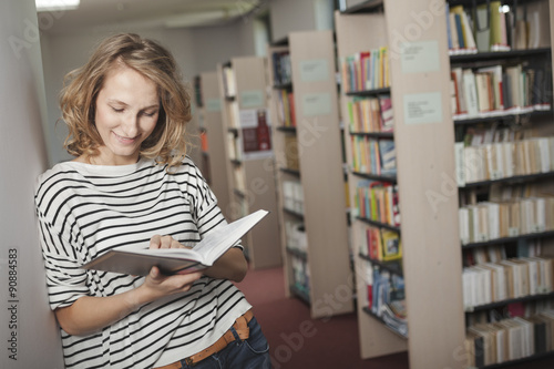 Portrait of clever student with open book reading it in college library
