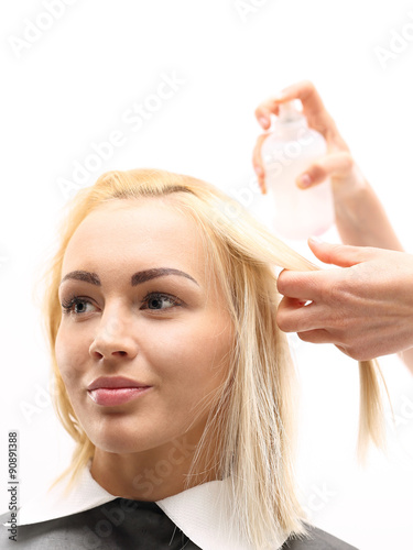 Fryzjer czesze piękną blondynkę, nakłada preparat zwiększający objętość włosów.