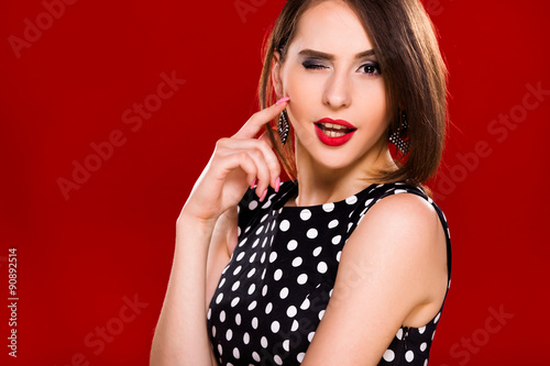 Flirtatious young woman is posing against a red background