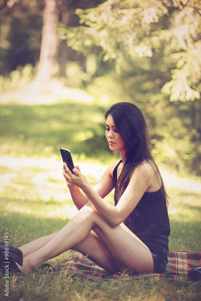 a beautiful young woman sitting at a picnic in nature and uses t