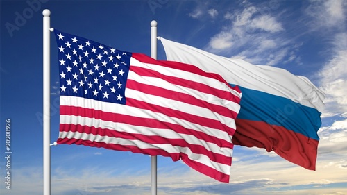 Waving flags of USA and Russia on flagpole, on blue sky background.