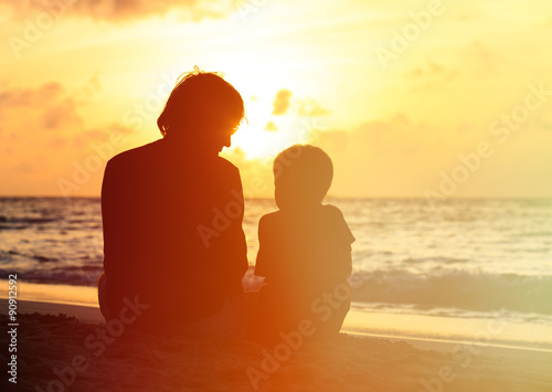 father and little son looking at sunset on beach