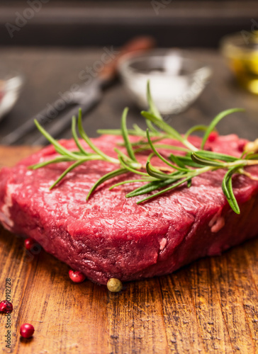 raw steak on a cutting board with a fork, rosemary, salt and oil on rustic wooden background, close up