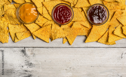 Mexican nacho chips and colorful dip in glass bowls on white wooden background, top view, horizontal border
