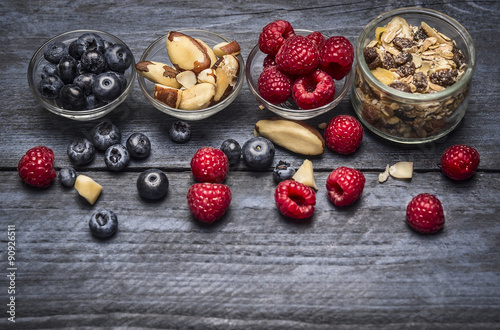 Glass bowls with ingredients for healthy breakfast - muesli berries and nuts on blue rustic wooden background