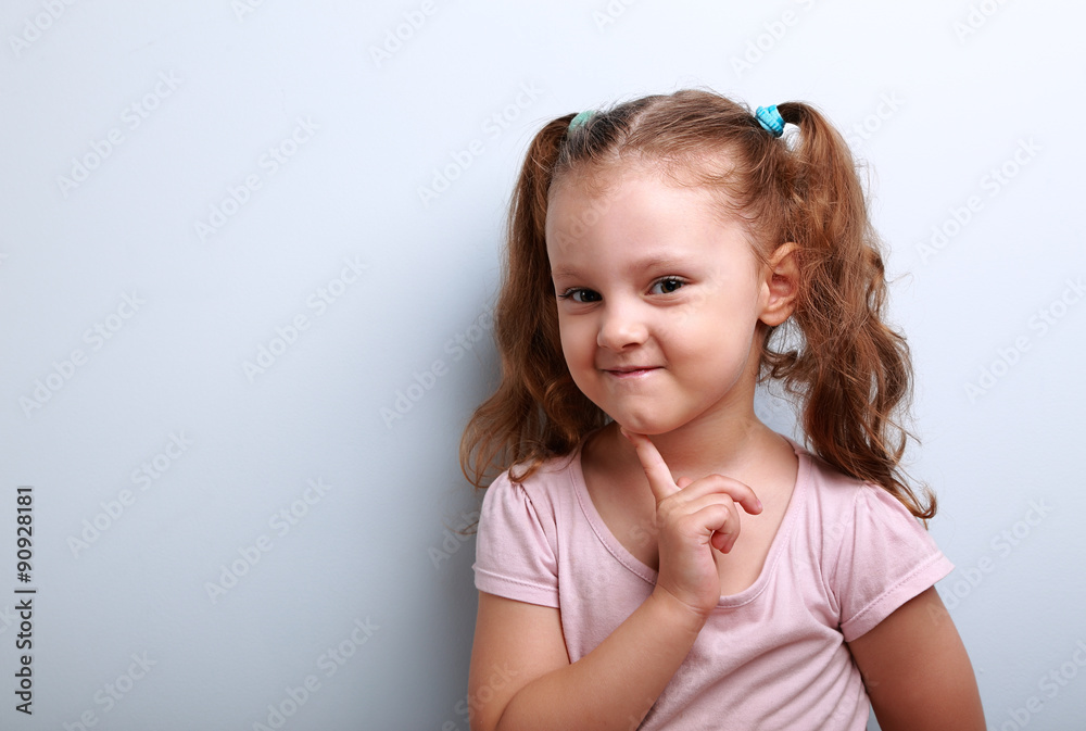 Cunning thinking small kid girl with finger near face on blue ba Cunning thinking small kid girl with finger near face on blue ba