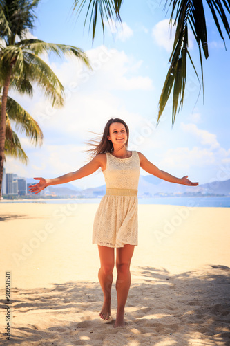 slim girl in white frock poses with hands aside on beach