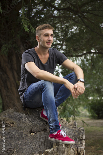 Young blond hipster man sitting on wood log.