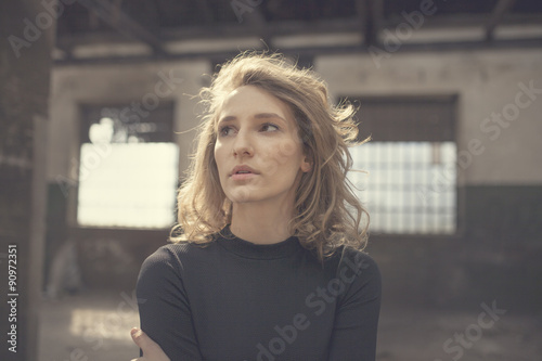 Beautiful woman with a serious expression on her face looking straight ahead with a view of abandoned building in the background