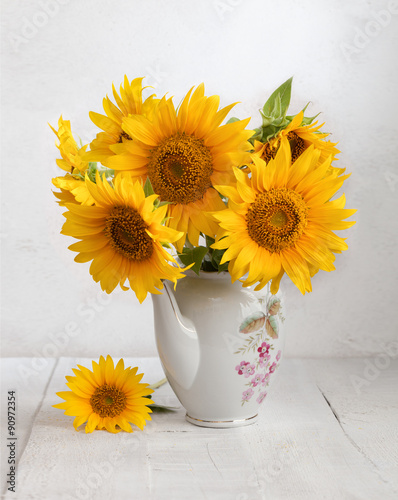 Fototapeta Naklejka Na Ścianę i Meble -  Bouquet of sunflowers in old ceramic jug against a white wooden wall.