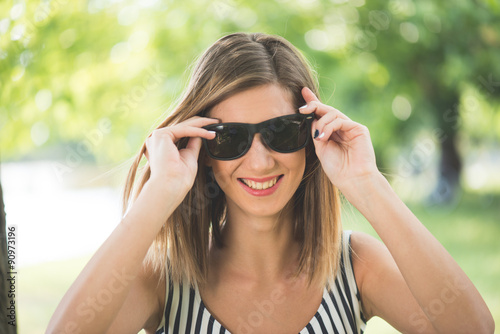 Summer portrait, young brunette woman playing with her sunglasses and having fun outdoor