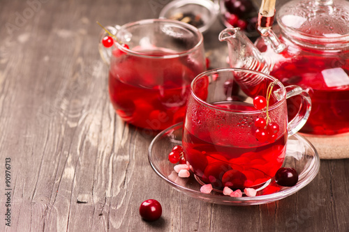 Hot berry tea in glass cups and teapot over rustic wooden background. 