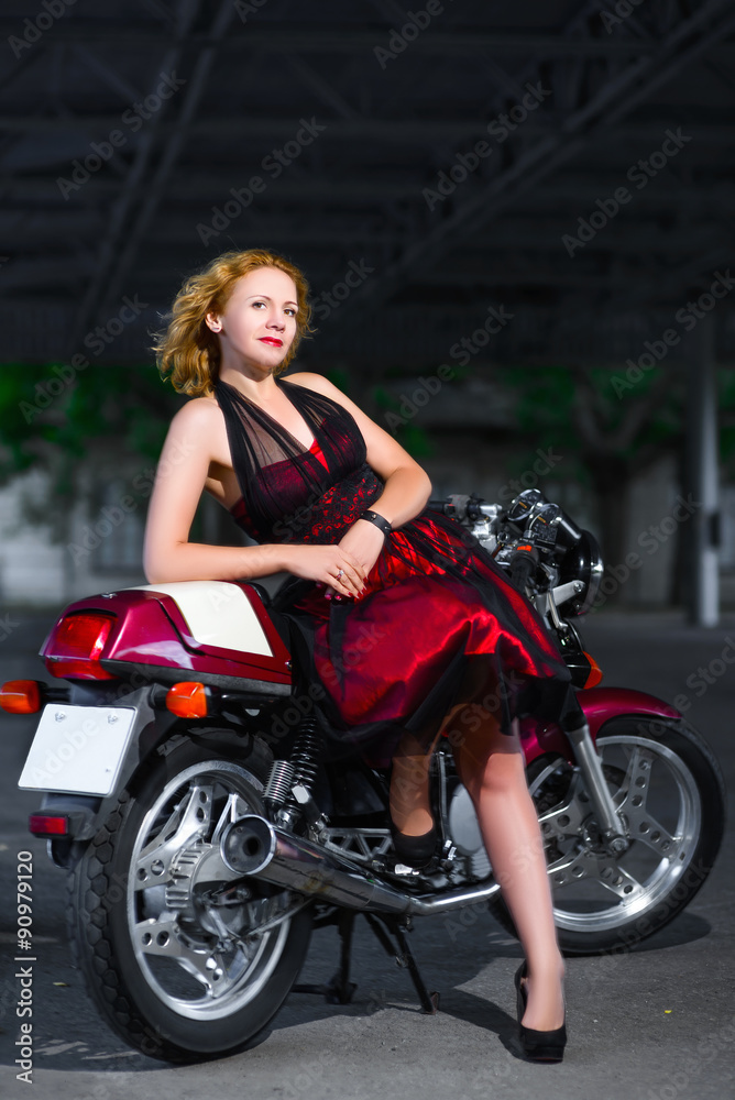 Biker girl in dress on a motorcycle over the background of dark