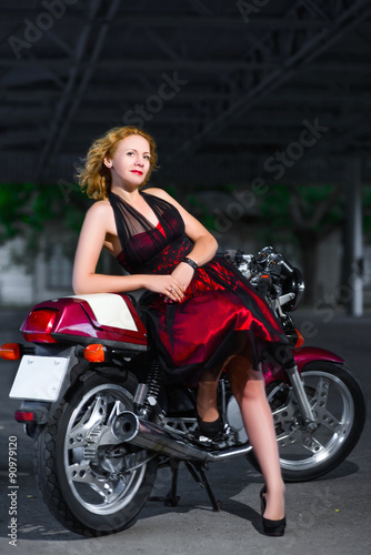 Biker girl in dress on a motorcycle over the background of dark