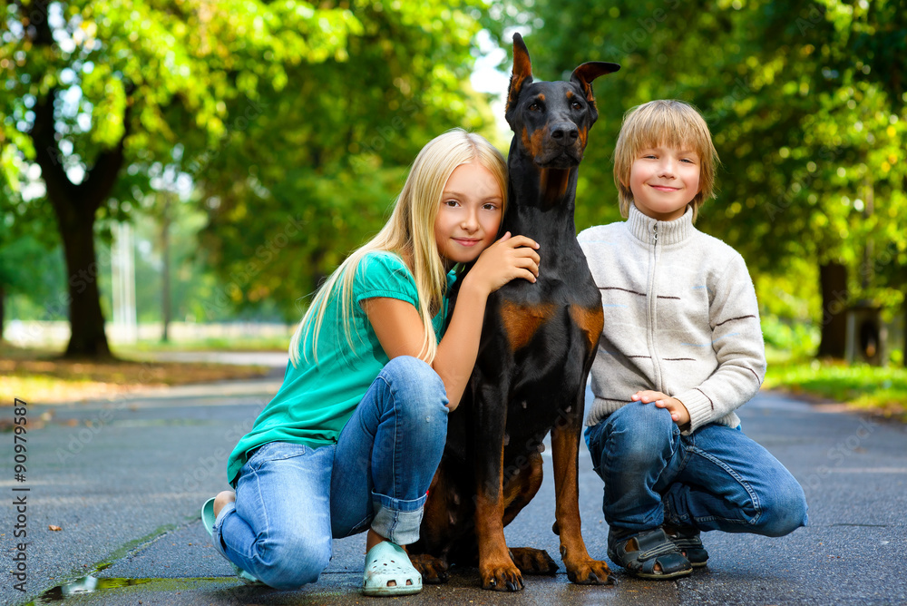 Fototapeta premium blonde girl and boy hugs beloved dog or doberman in summer park
