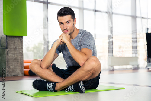 Fitness man sitting on yoga mat at gym