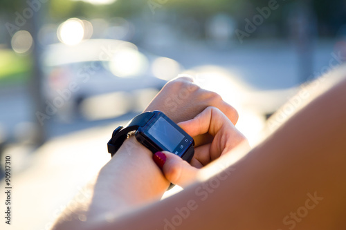 Beautiful young woman using her smartwatch in the street.