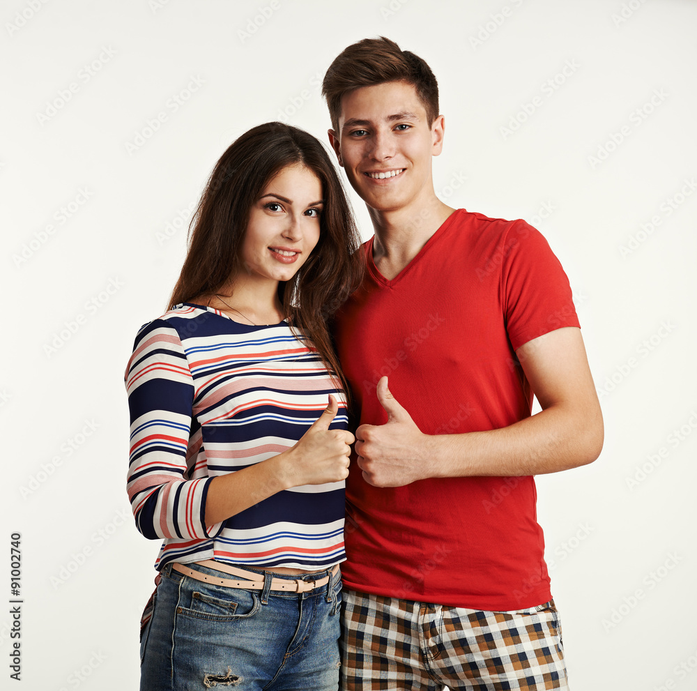Studio shoot of smiling young couple showing thumb up gesture. Two stylish teenage people embracing indoors. Studio shoot of smiling young couple showing thumb up gesture. Two stylish teenage people embracing indoors.